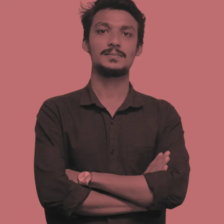 Young man with moustache and beard in a dark shirt with arms crossed, wearing a watch.