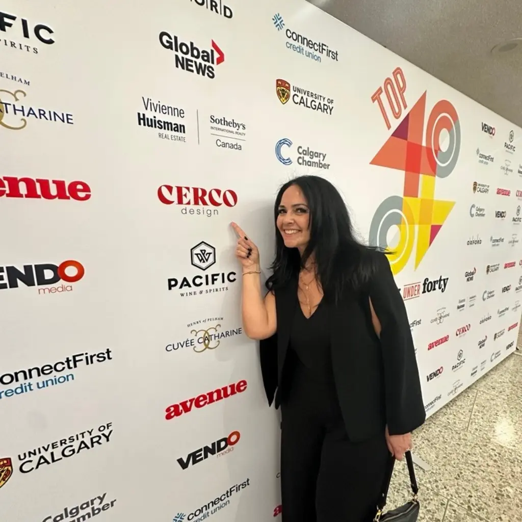 Woman points to CERCO design logo on a backdrop of sponsors' logos at an event.