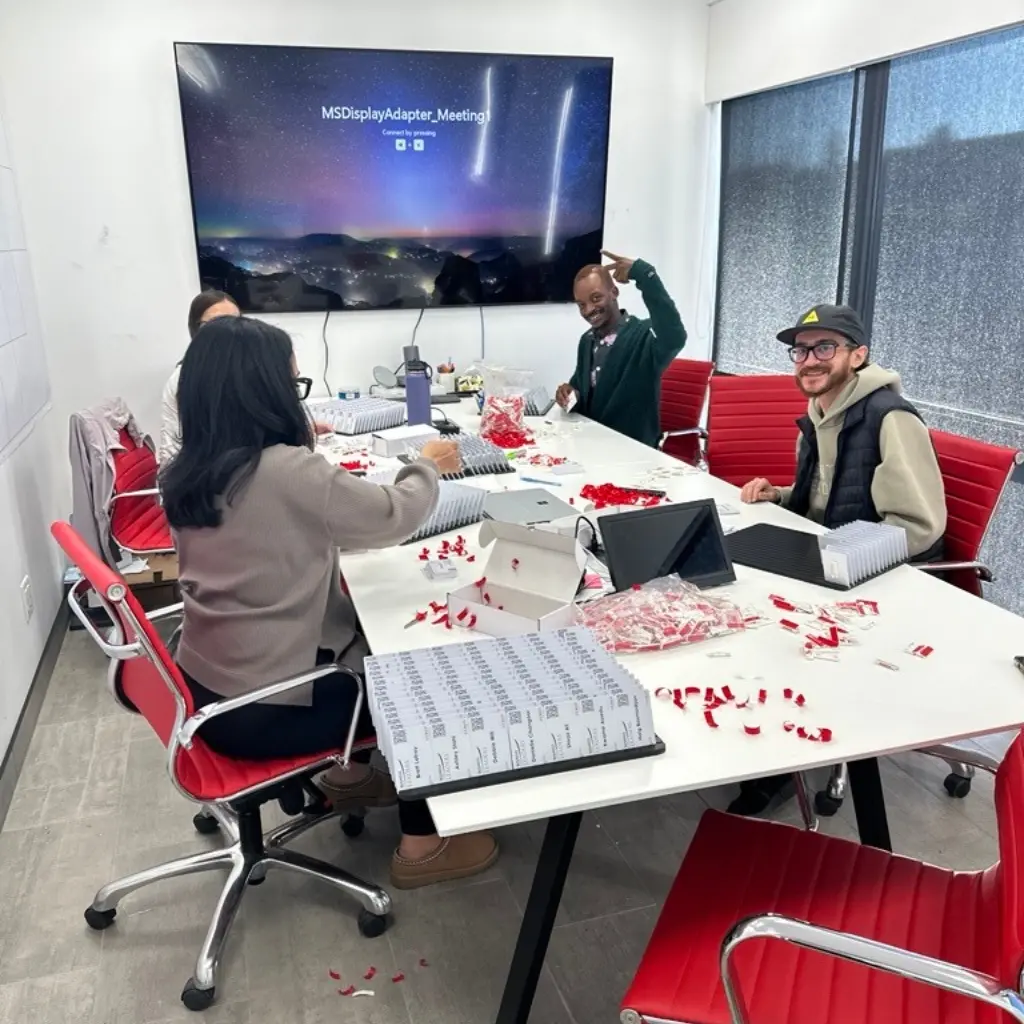 Team assembly of small electronic components around a conference table with a display showing MSDisplayAdapter Meeting.
