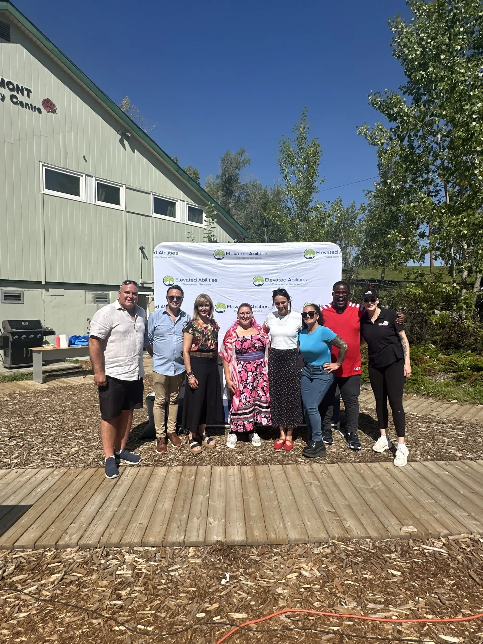 Group of people pose in front of banner for Elevated Abilities Therapeutic Services and a building.