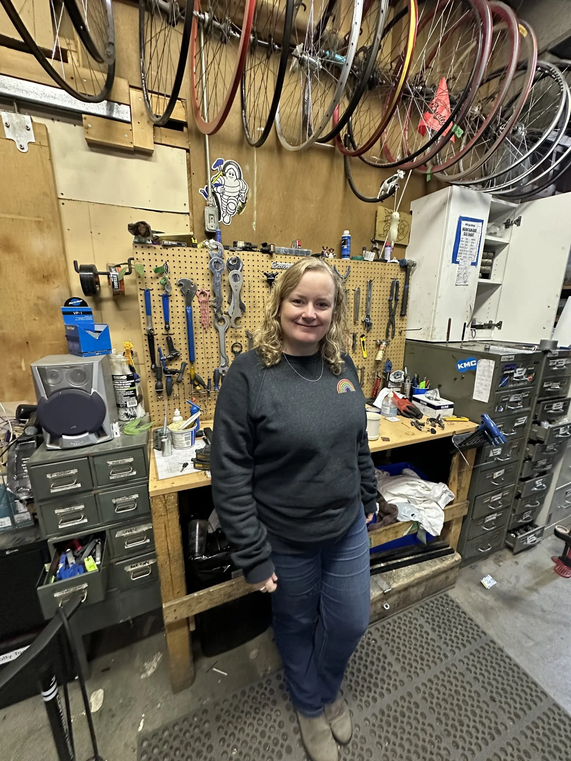 Woman in bike shop with wheels hanging above tool wall