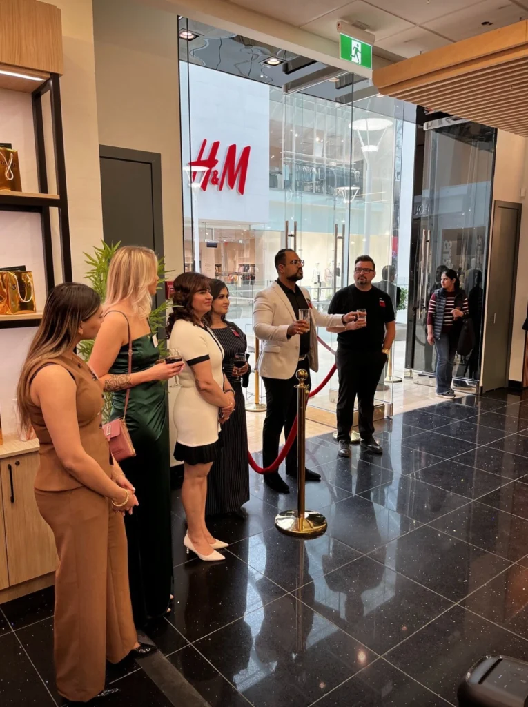 People gathered inside an H&M store for an event, with a velvet rope barrier in the foreground.