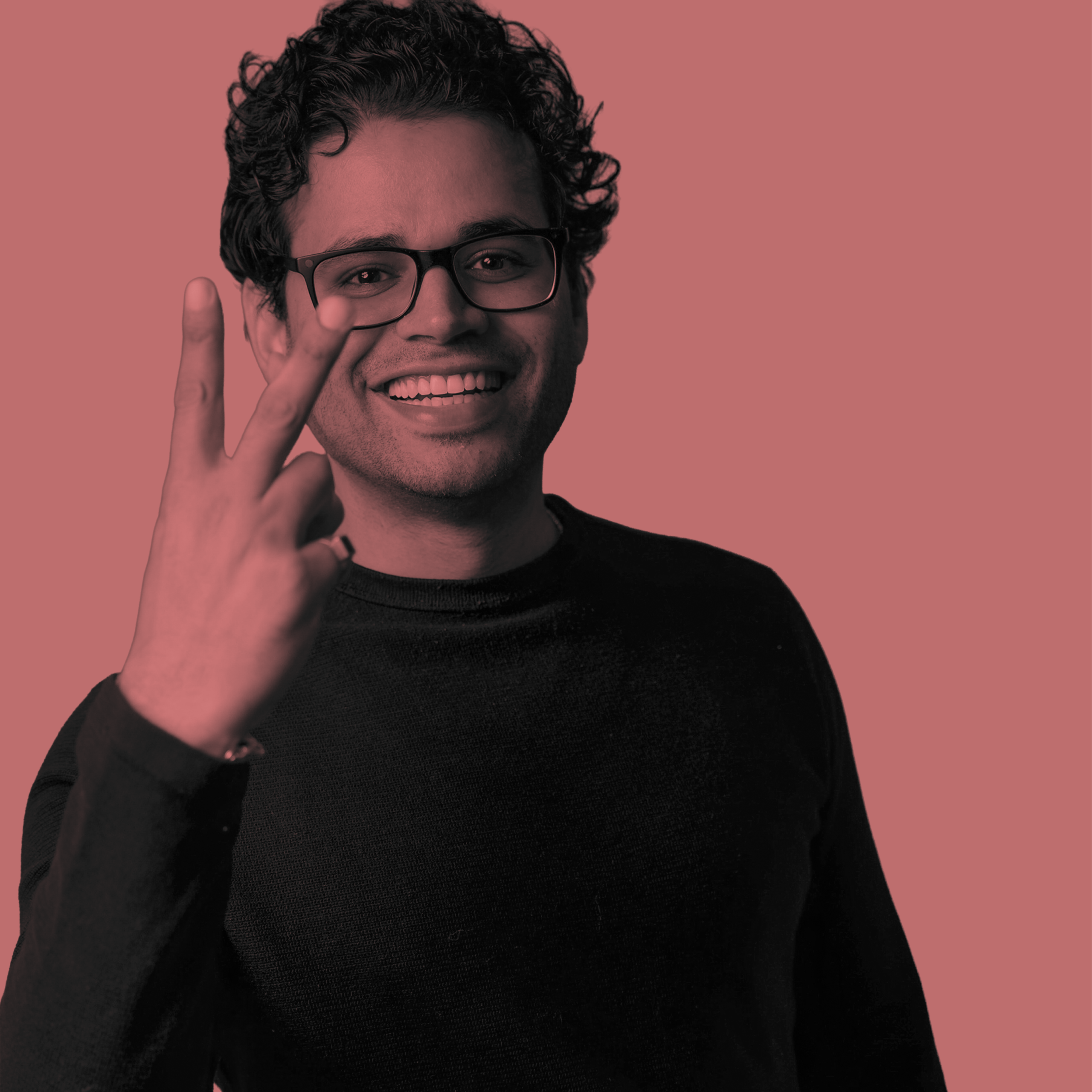 Smiling man with glasses holds up two fingers in a peace sign.