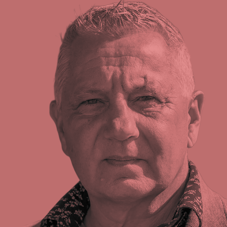 Close up portrait of an older man's face, light-skinned, grey hair, wearing a patterned shirt.