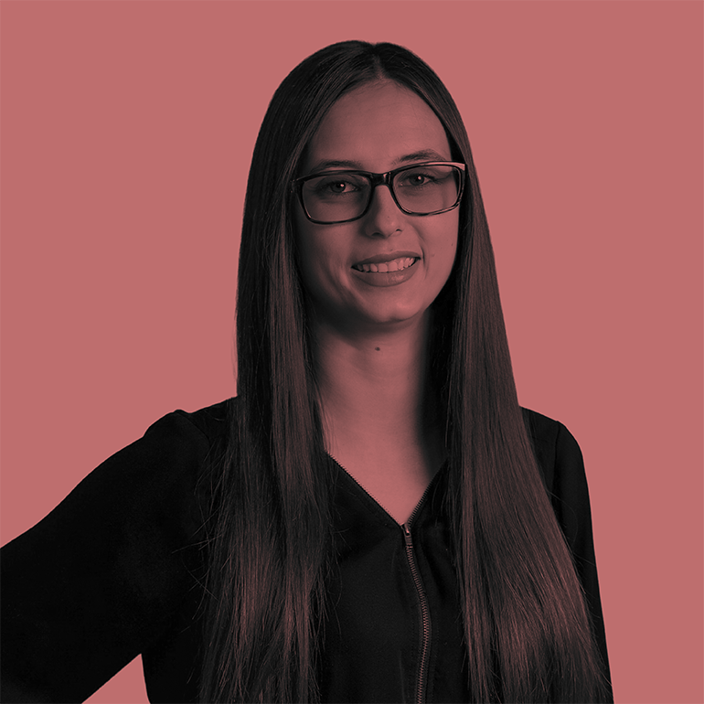 Woman with long brown hair and glasses in black top smiling against pink background.